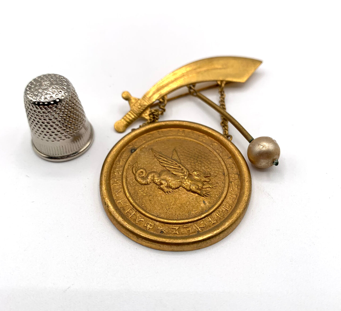 Broche vintage de metal dorado con forma de gong, dragón y espada