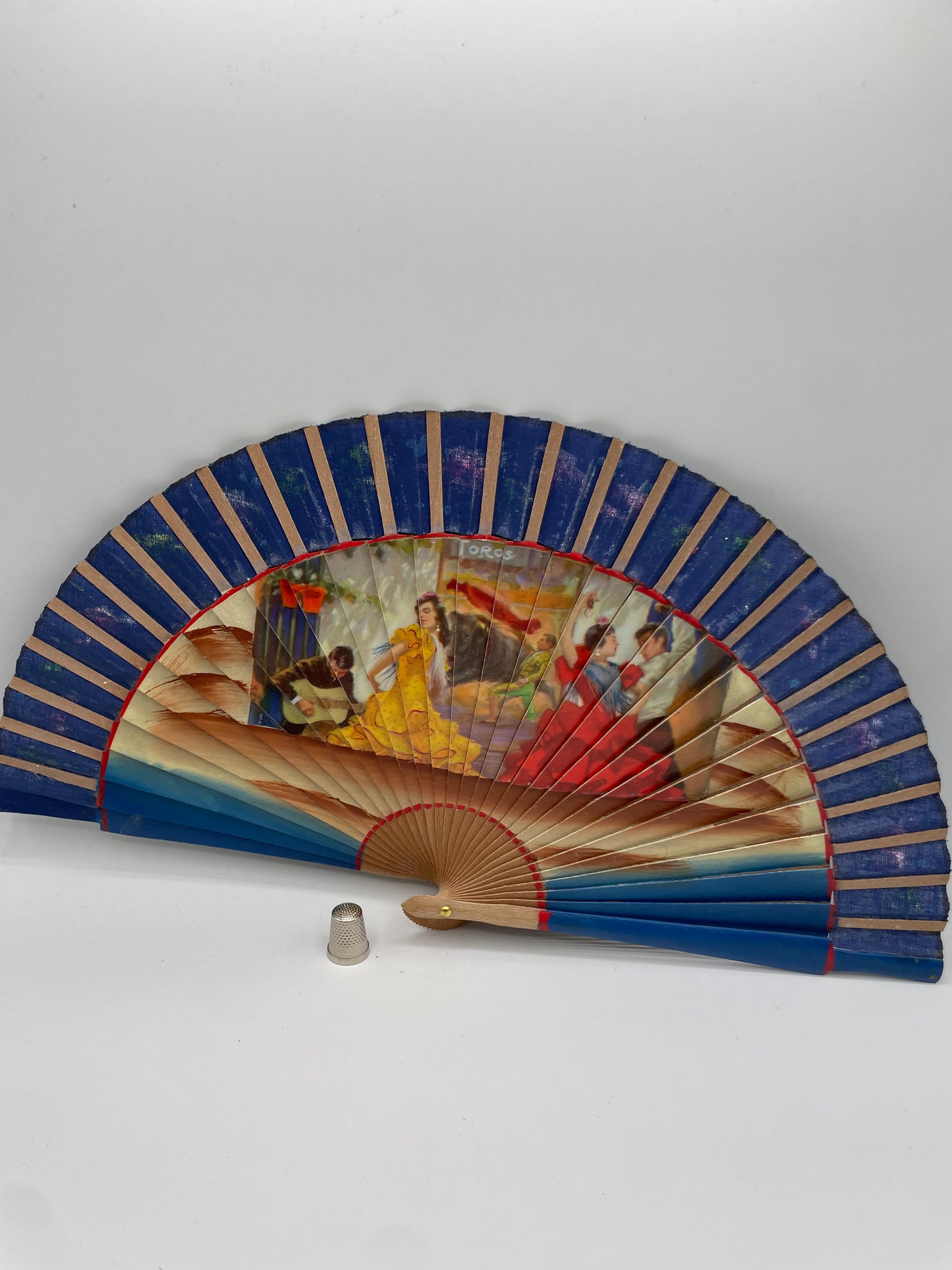 Abanico de madera, color azul, pintado a mano con coloridas flores e imagen impresa de escenas flamencas por ambas caras