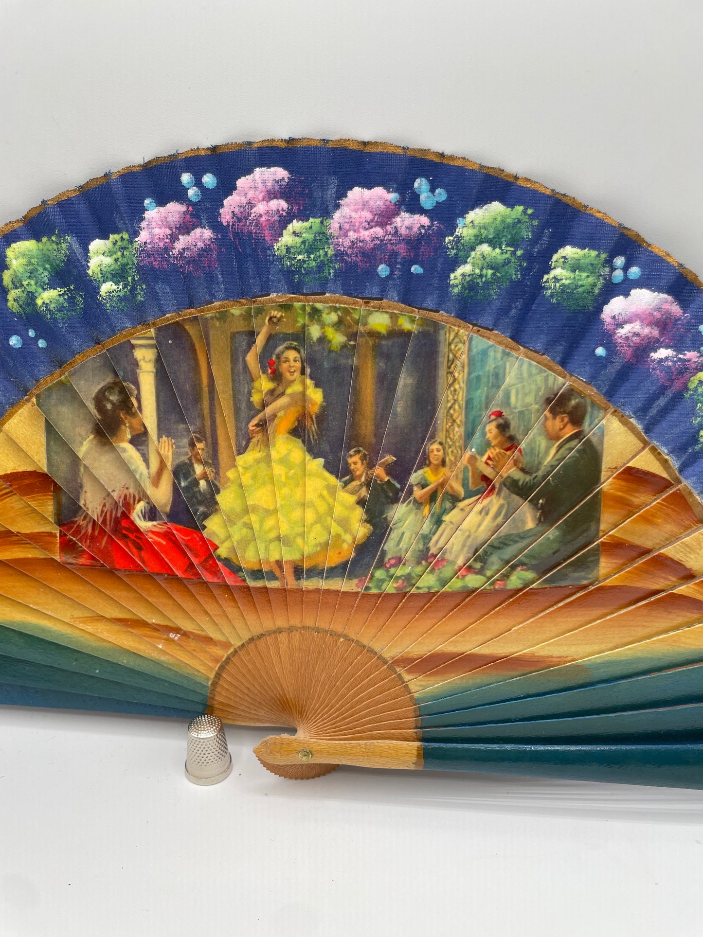 Abanico de madera, color azul, pintado a mano con coloridas flores e imagen impresa de escenas flamencas por ambas caras